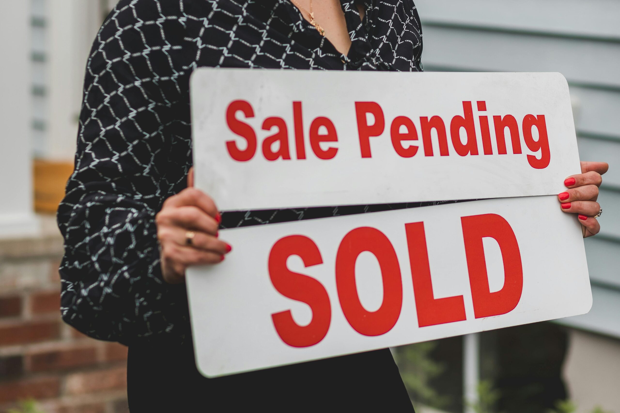 Woman holding red Sale Pending and Sold signs.