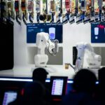 a group of people watching how two robotic arms perform bartender tasks